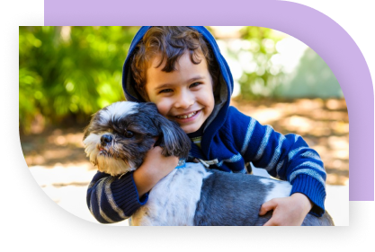 A young boy holding a black and white dog and smiling.