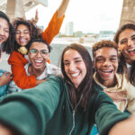 Young adults taking a selfie, all smiling and laughing toward the camera. A group with healthy teen independence.