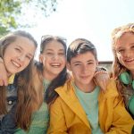Four pre-teens lined up with arms around each other and smiling. Social skills development focus image.
