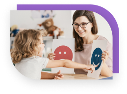 A child pointing at a smiley face that is being held up by a therapist. The therapist has a sad face in her other hand.
