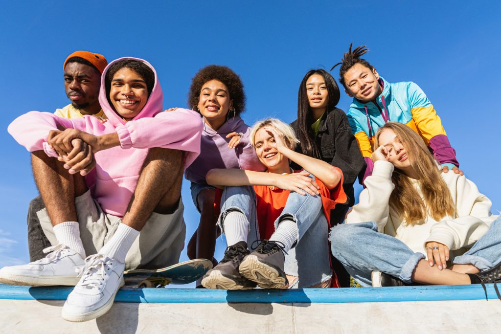 Teens sitting on a wall in the sun. they are mostly smiling, but all looking at the camera and posing.