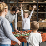 Family around a foosball table, the young daughter celebrating by throwing her hands in the air.