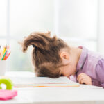 A young girl with her head down on a table, face down.