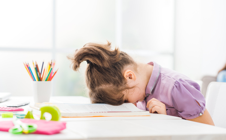 A young girl with her head down on a table, face down.