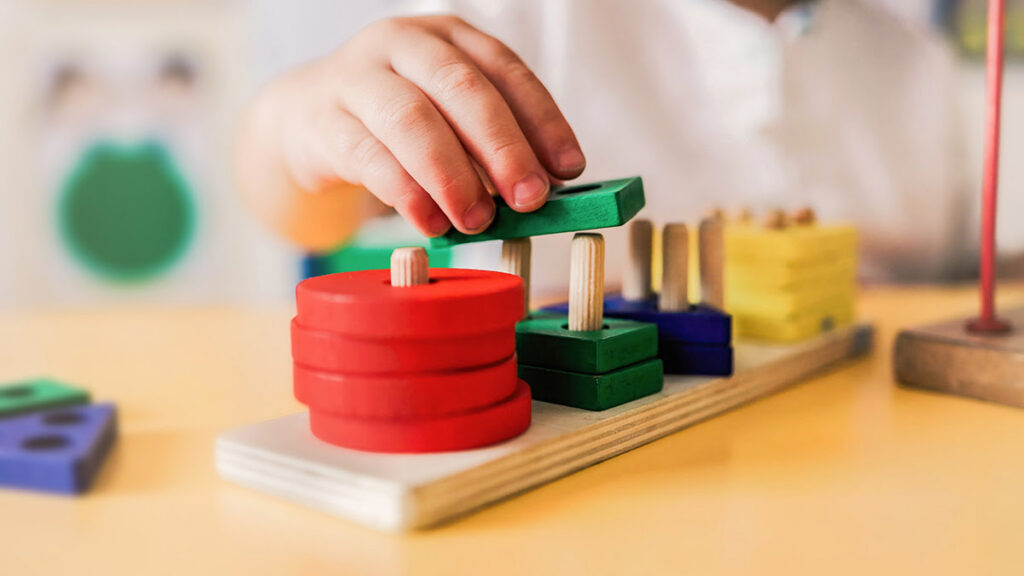 Image of a stacking toy with a child's hand stacking a piece on it.