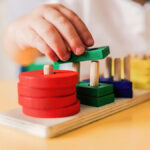 Image of a stacking toy with a child's hand stacking a piece on it.
